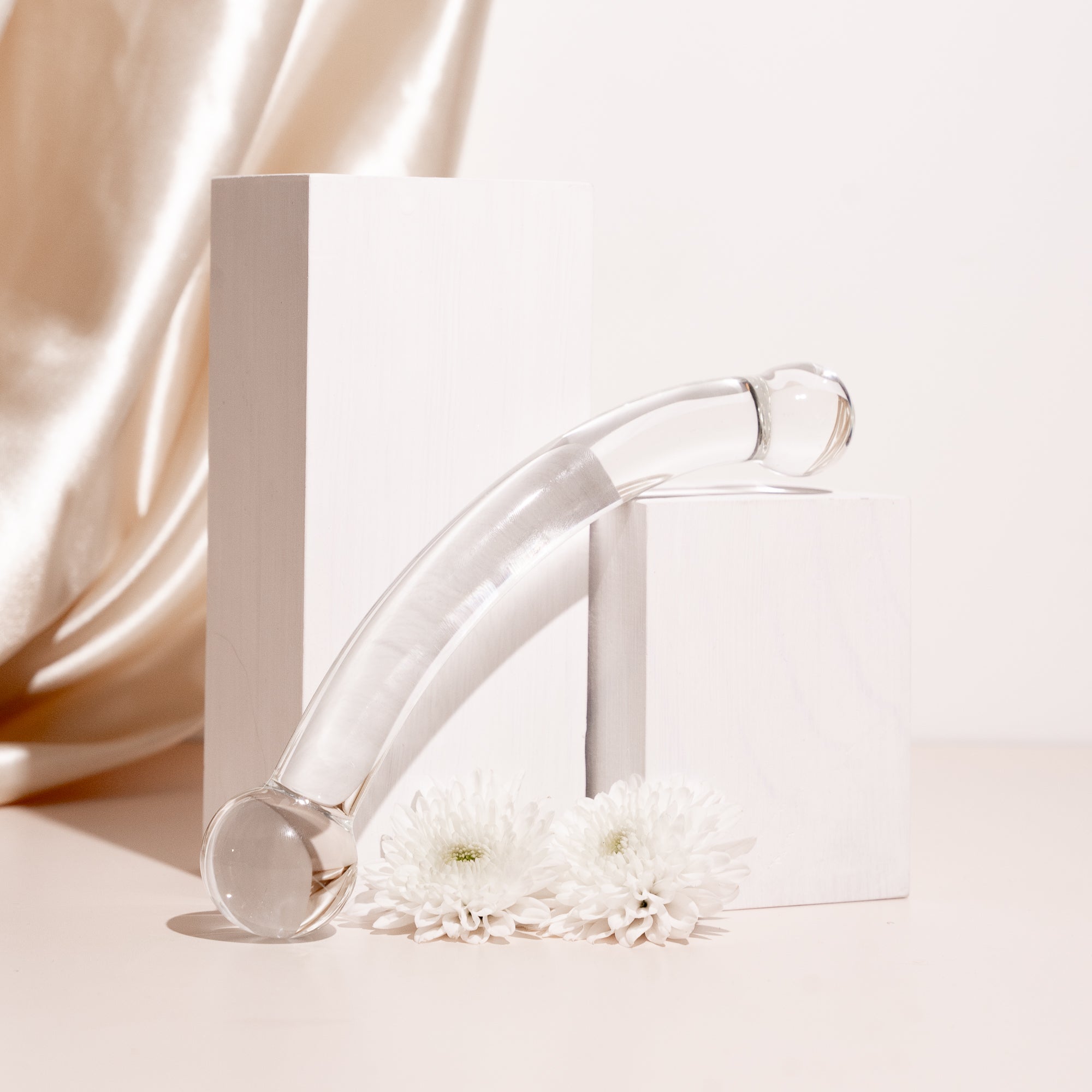 Curved clear glass pleasure wand with thicker spherical heads. Pictured on stone blocks with flowers and champagne coloured background.