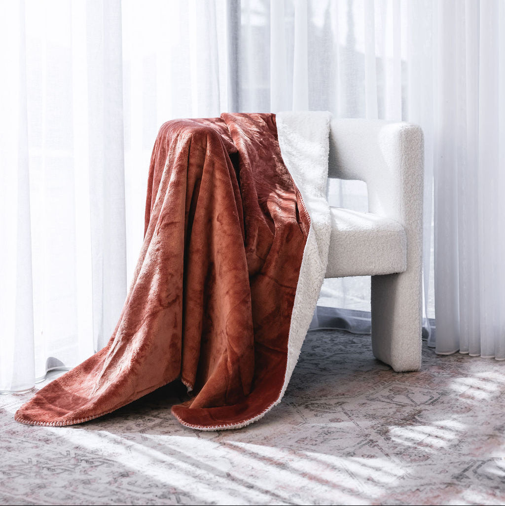 A plush throw blanket draped over a modern white armchair in a bright room with sheer white curtains and sunlight streaming through.