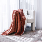 A plush throw blanket draped over a modern white armchair in a bright room with sheer white curtains and sunlight streaming through.